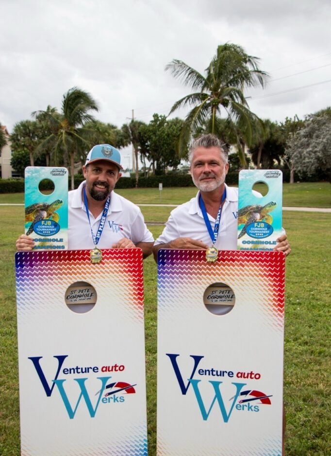Two men with awards at cornhole tournament.